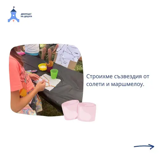 Момиче нарежда солети и маршмелоу в очертанията на съзвездие върху маса с тъмна покривка на открито.