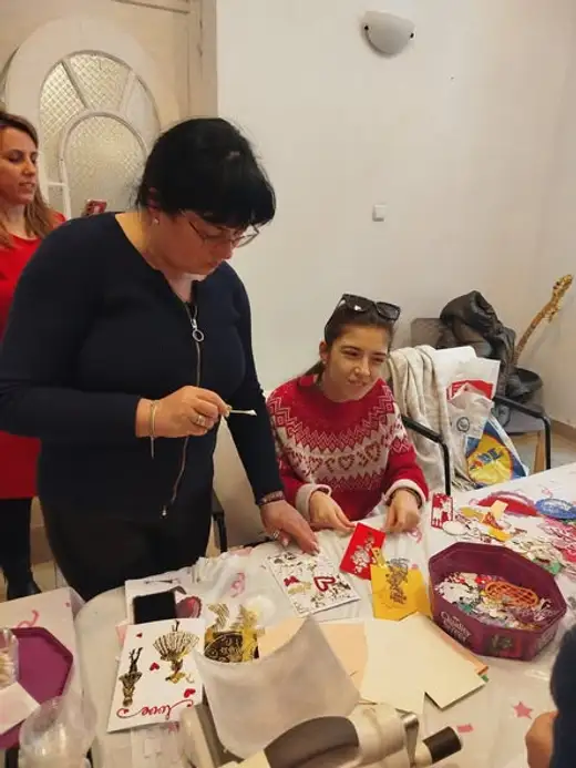 Две жени и момиче работят на маса, пълна с хартия и части за изработка.