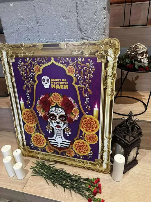 Плакат на фестивала с рисувана женска фигура с цветя в позлатена рамка, около него свещи, червени карамфили и малка глава на череп.