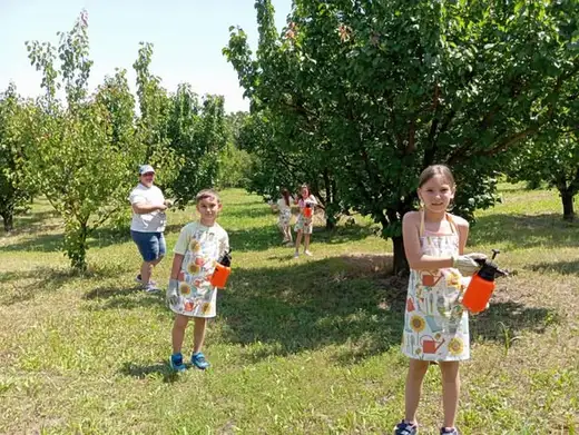 Три деца с пръскачки вървят между дърветата.