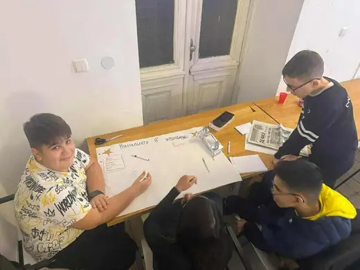 Ученици се навеждат над маса с вестници и голям бял лист.