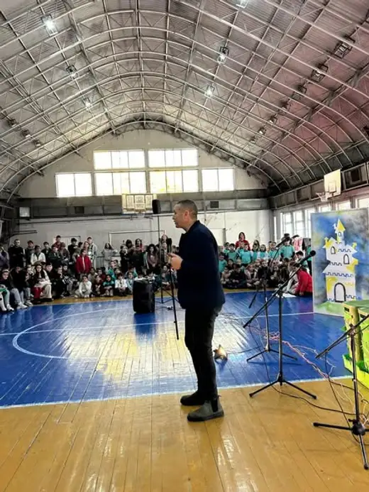 Мъж говори с микрофон в средата на спортния салон.