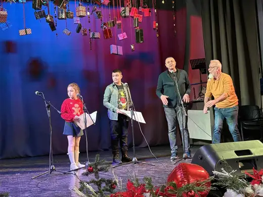 Момиче с лист в ръка и двама мъже на сцената.