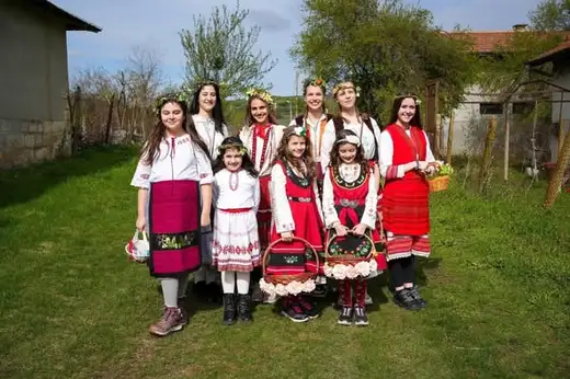 Голяма групова снимка на момичета в носии и с кошници пред селска къща.