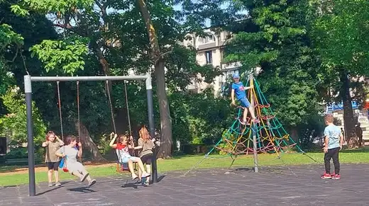 Деца се люлеят на детска площадка сред дървета