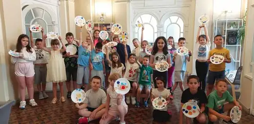 Деца показват кръгли палитри с бои в светлата зала