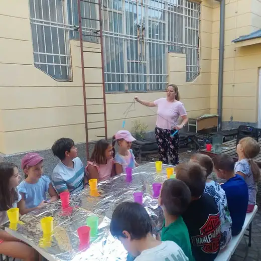 Деца в двора около маса с цветни чашки
