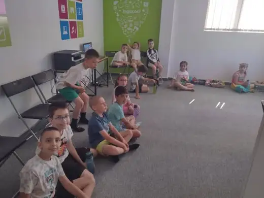 Деца, седнали на пода, слушат презентация в светла зала