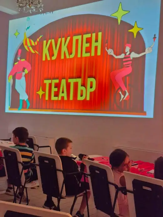 Проектиран екран „Куклен театър“ пред редици столове в залата