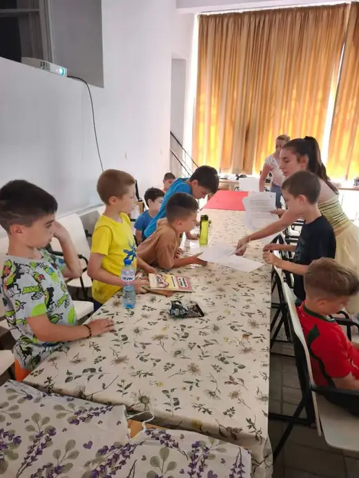 Деца работят на дълга маса с покривка на лавандула