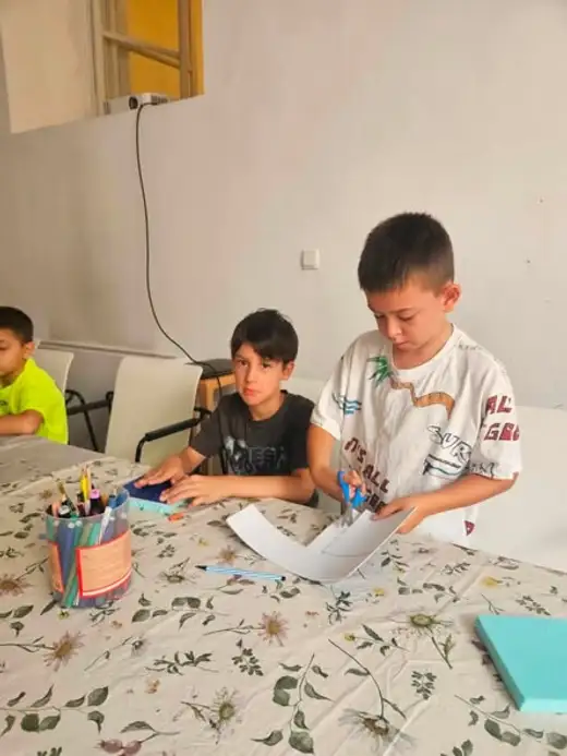 Две момчета изрязват и подреждат цветна хартия на масата