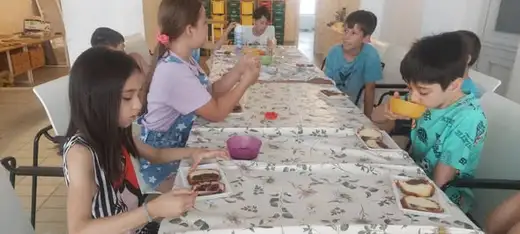 Деца хапват на дълга маса, покрита с шарена покривка.