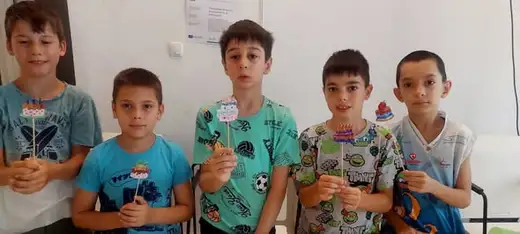 Петима момчета стоят до бяла стена и държат малки изработки от хартия.