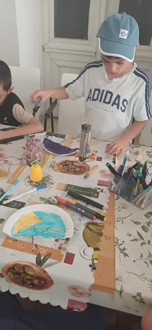 Момче оцветява чиния на маса с четки, бои и хартии