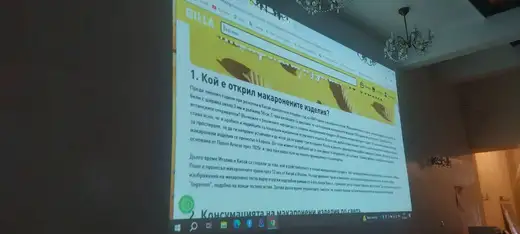 Проектирана на стената презентация за историята на макароните в зала с полилей.