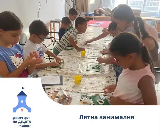 Деца оформят глинени изделия на дълга маса със зелени подложки, долу вляво е логото на лятната занималня.
