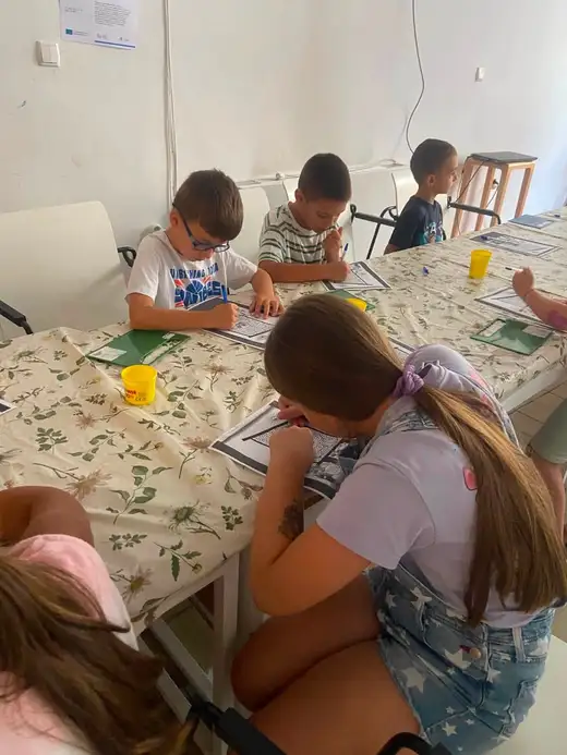 Деца седят край маса и работят с бяла глина върху зелени подложки.