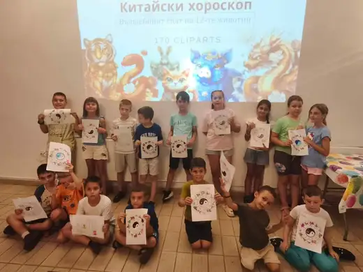 Група деца държат рисунки пред проектиран на стената „Китайски хороскоп“.