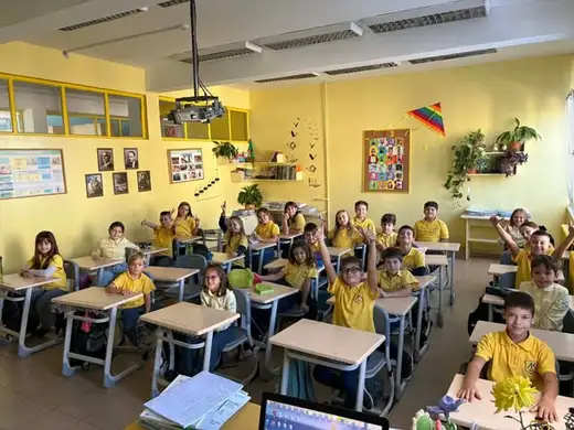 Класна стая с ученици по чиновете, обърнати към камерата.