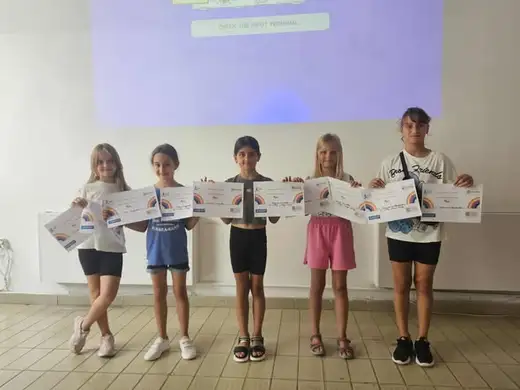 Пет деца държат сертификати пред прожектиран екран.
