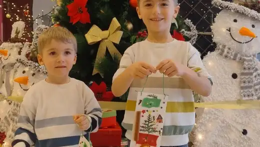 Момче до голяма фигура на снежен човек държи готовото си коледно пано с панделка.