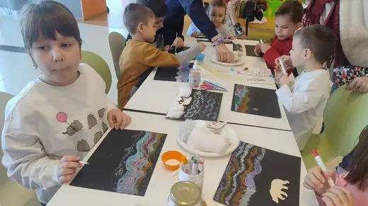 Деца и родители работят край масите в мола до панорамния прозорец.