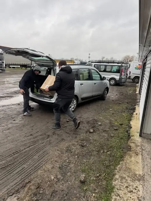 Мъже товарят кашони в багажник на автомобил.