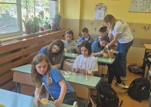 Ученици сглобяват конструкции по чиновете, а жена им помага.