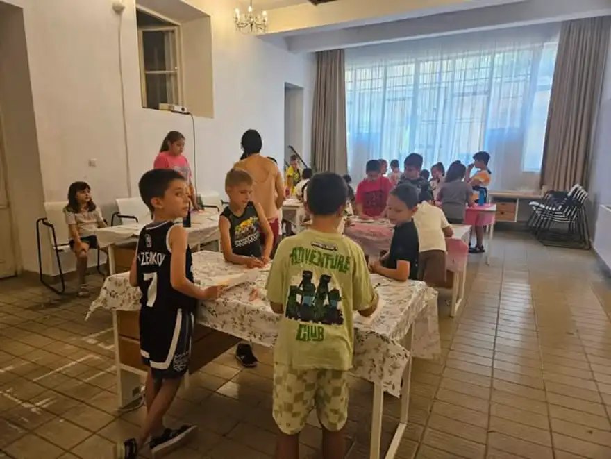 Деца работят на групи около маси в залата на центъра.
