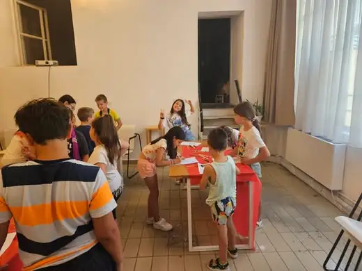 Деца се събират около високи маси в залата.