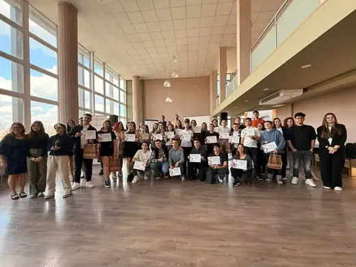 Голяма групова снимка на участниците във фестивала в зала с големи прозорци.