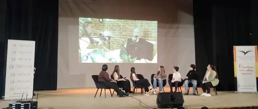Участници в разговор на сцената, зад тях екран с изображение.