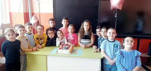 Група деца стоят до маса в класната стая.