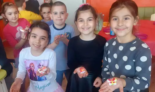 Деца се усмихват към камерата и държат малки предмети в ръце.