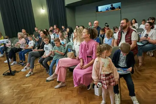 Родители и деца седят в залата по време на церемонията.