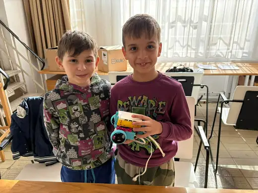 Две момчета показват сглобен жълт робот.