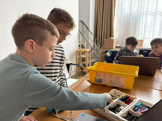 Момче се навежда към кутия с детайли, до него се вижда още едно дете.