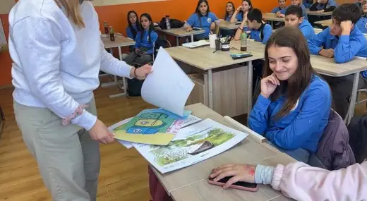 Ученичка държи нарисуван лист пред съученици на чиновете.