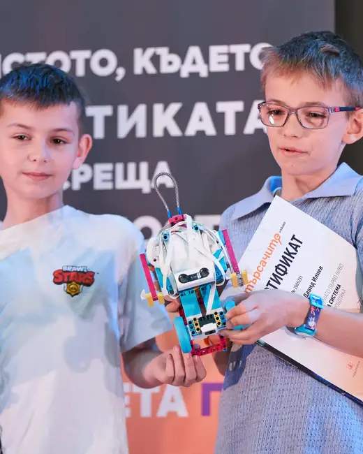 Две момчета пред тъмно пано: това вдясно, с очила, държи сглобен от LEGO робот с антена и сертификат.