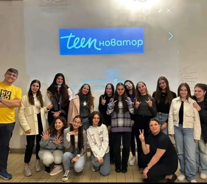 Група младежи и двама ментори позират пред екран с логото на Teenovator.