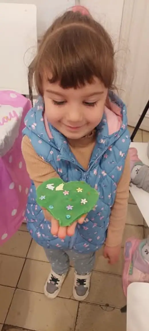 Момиче държи изработена зелена фигура от глина.
